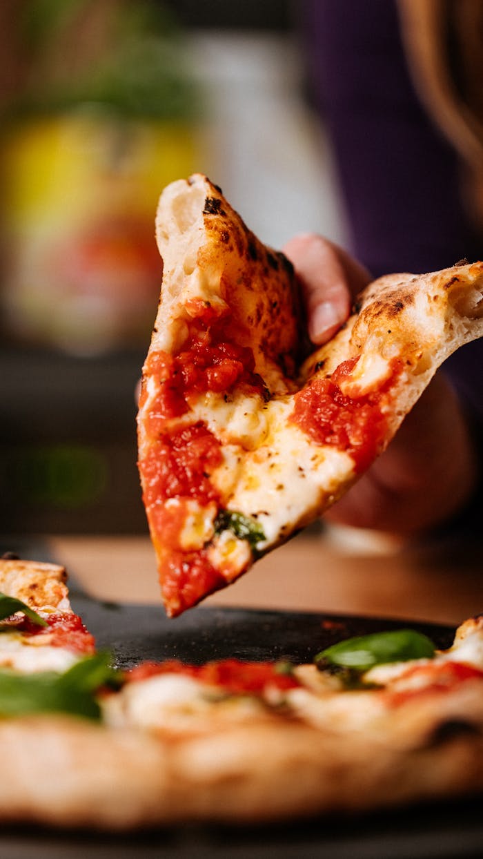 Close-up of a hand holding a vegan pizza slice with fresh mozzarella and basil.